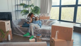 Young happy diverse couple from Caucasian man and African American woman resting after moving into apartment rented for long time or bought for living together sits on sofa among boxes in living room. - Powered by Shutterstock - Get 15% off with code: PIKWIZARD15