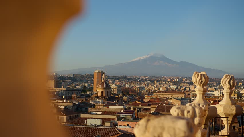 View of Mount Etna towering behind Catania’s historic city center during golden hour in Sicily, Italy