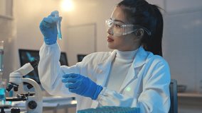 Young scientist wearing lab coat and protective glasses analyzing blue solution in test tube while working with microscope in modern laboratory. - Powered by Shutterstock - Get 15% off with code: PIKWIZARD15
