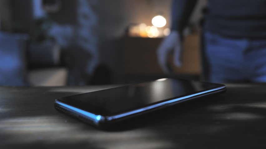 male picking up mobile phone from table at night,person at home picks up smartphone from the desk in the dark room