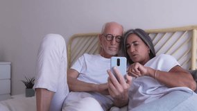 Elderly couple relaxing in bed, browsing social media or online shopping on smartphone. 4k resolution video. - Powered by Shutterstock - Get 15% off with code: PIKWIZARD15