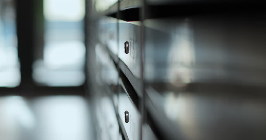 Close-up woman is opening her mailbox inside a cluster of mailboxes for her apartment. Mail shipping concept.