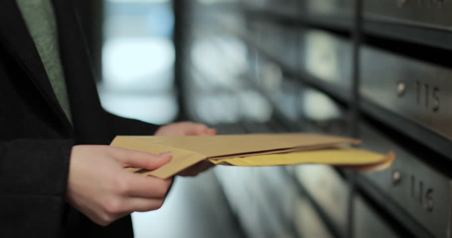 Close up woman is opening her mailbox inside a cluster of mailboxes for her apartment. Payment notification letter. Mail shipping concept.