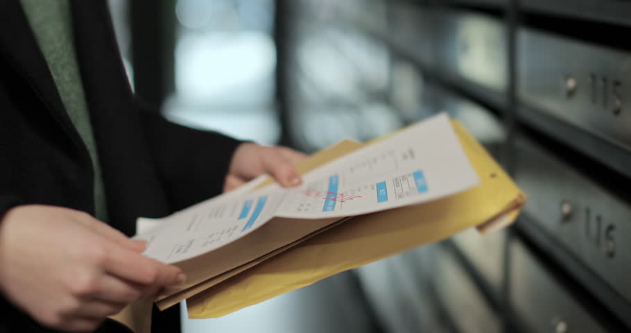 Close up woman is opening her mailbox inside a cluster of mailboxes for her apartment. Payment notification letter. Mail shipping concept.
