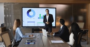 Group of businesspeople sit around table listening speech of boss, engaged in formal business meeting, presentation, or strategy, digital screen displaying detailed charts, and graph behind presenter - Powered by Shutterstock - Get 15% off with code: PIKWIZARD15