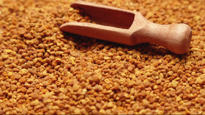 A small wooden scoop on a pile of bee pollen granules