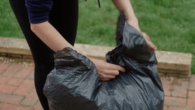 Woman tying garbage bag filled with collected leaves. Female securing trash bag after outdoor cleaning. Housewife closing bag of yard debris after tidying patio. Lady managing cleanup by sealing bag - Powered by Shutterstock - Get 15% off with code: PIKWIZARD15