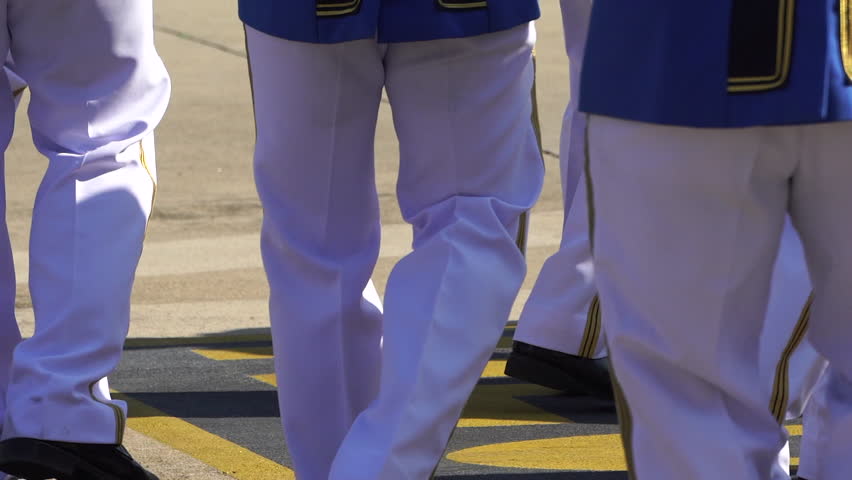A row of soldiers in white uniforms marching and playing drums.