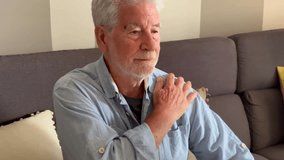 Retired man with a painful expression sitting on a couch at home, massaging his neck and shoulder to relieve tension caused by aging, stress, exhaustion, and the physical demands of daily life - Powered by Shutterstock - Get 15% off with code: PIKWIZARD15