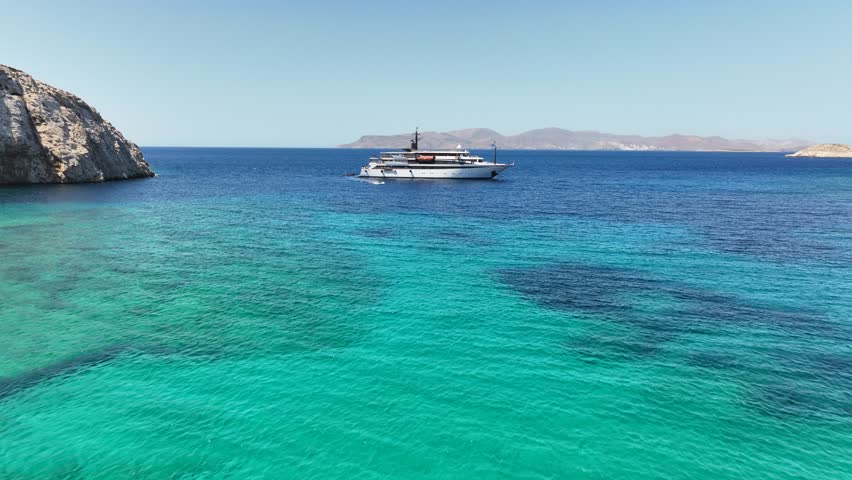 Aerial drone cinematic video of luxury yacht anchored in tropical exotic island bay with two sided sandy beach with emerald crystal clear sea