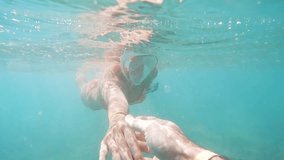 under the surface of the sea, a young woman in an orange and white bathing suit is swimming, and she reaches out to grab the cameraman's hand, then peers into the water with her diving mask. - Powered by Shutterstock - Get 15% off with code: PIKWIZARD15