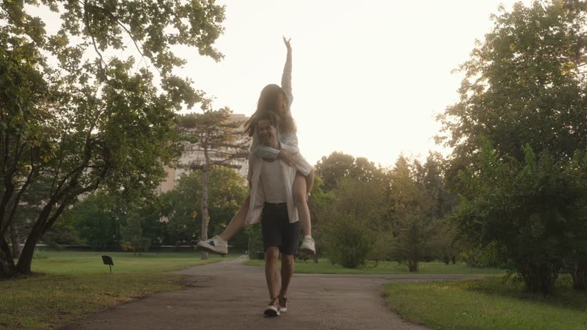 Romantic video of a young couple having fun at the park. The man is giving the woman a piggyback ride as they both smile and laugh.
