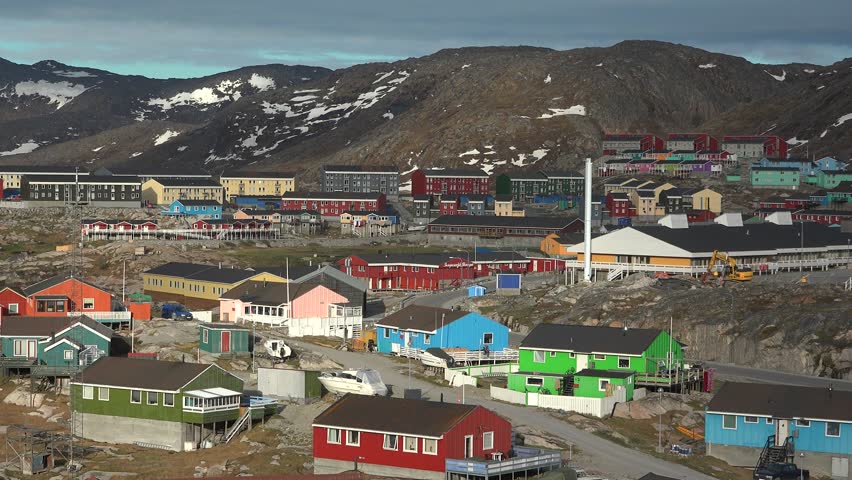 Colorful houses dot the coastal landscape of Greenland with distant icebergs on a clear day