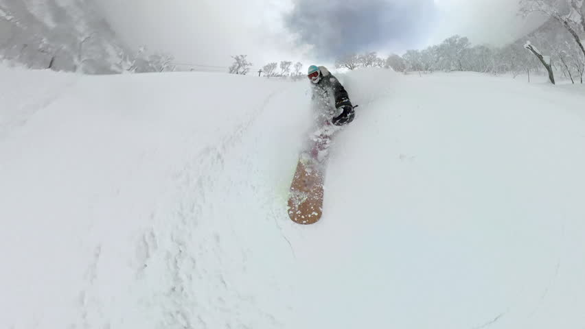 SELFIE: Snowboarder sprays clouds of fresh snow while riding off the ski slope. White frosted trees, deep powder and smiling face capture the thrill of backcountry snowboarding in Japanese mountains.