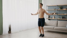 A sporty young man is jumping rope in his living room, focusing on his workout. The bright space features a couch and shelves, highlighting his commitment to a healthy lifestyle. - Powered by Shutterstock - Get 15% off with code: PIKWIZARD15