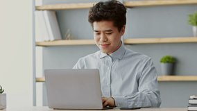 A young Asian man engages in remote work at his home office, focused on his laptop. Natural light fills the room, highlighting his productive atmosphere and active engagement with his tasks. - Powered by Shutterstock - Get 15% off with code: PIKWIZARD15