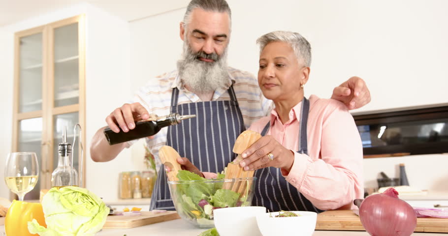 Senior couple preparing salad together, pouring olive oil and mixing ingredients. Cooking, kitchen, healthy eating, vegetable, meal prep, bonding