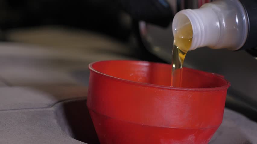 Oil change in the car. Close-up of a mechanic pouring new engine oil into the engine. Replacement of technical fluids of the car in the car repair shop.