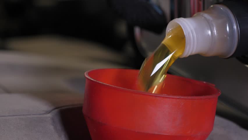 Oil change in the car. Close-up of a mechanic pouring new engine oil into the engine. Replacement of technical fluids of the car in the car repair shop.