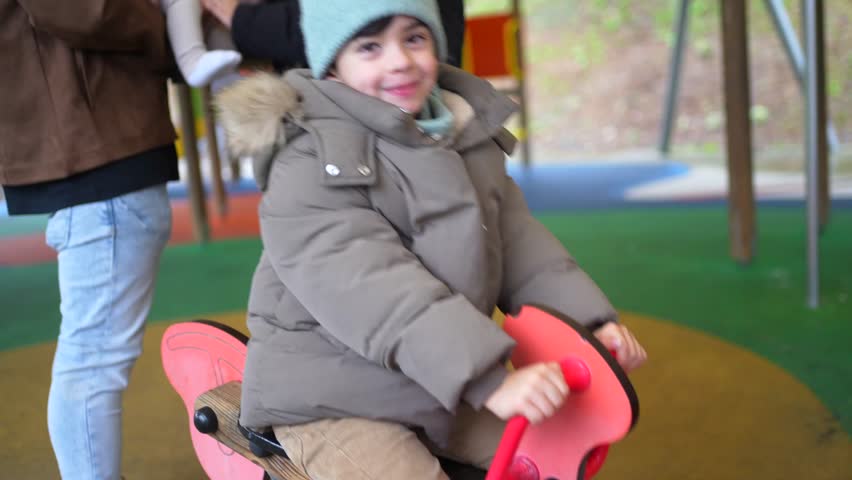 Young boy having fun riding a rocking horse at a playground during winter, surrounded by family
