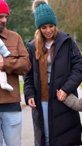 Warm winter atmosphere capturing family walking together, parents holding baby's hand and smiling while enjoying peaceful park scenery during cold season