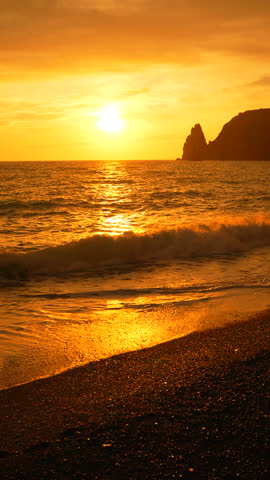 Vertical Aerial view Sunset Ocean Beach: Golden hour seascape, dramatic coastal rock formation at sunset, peaceful ocean waves.