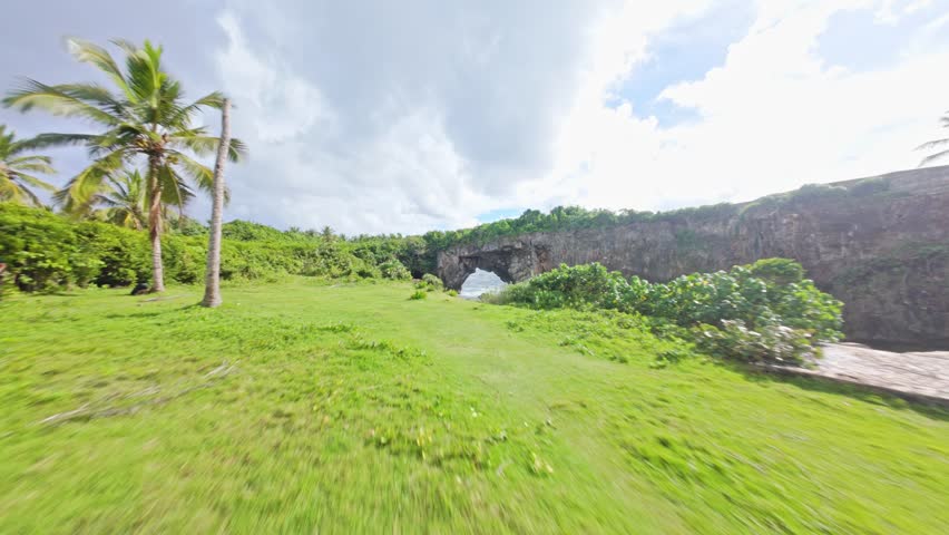 FPV drone flight through natural arch with Caribbean Sea during sunny day. LA HONDONADA, LAS GALERAS SAMANA. Cloudy day and coastline