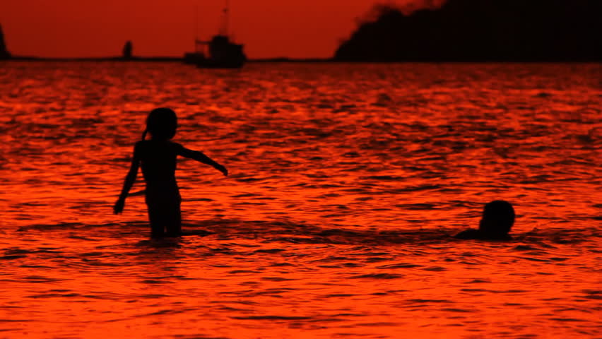 Silhouettes of children playing in the surf of Playas del Coco during sunset in