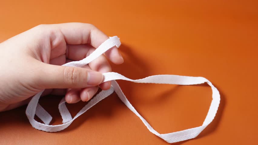 Hand tying simple knot on white cotton fabric string object footage isolated on horizontal brown background.