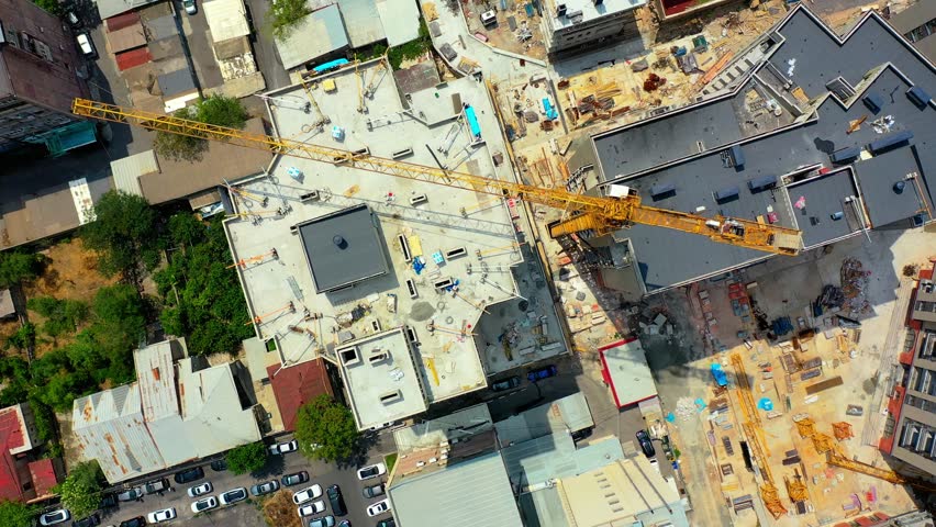 Top view towering crane at construction site.  Aerial view captures ongoing construction work in a bustling urban environment. A large crane dominates the skyline while workers and machinery are busy 