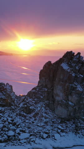 Aerial view of Shaman rock at sunset, one of sacred place in frozen lake Baikal in winter season of Siberia, Russia. Vertical video