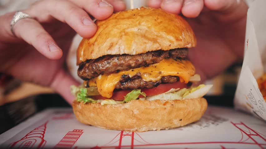 Juicy freshly cooked cheeseburger close-up, hungry man picks up the burger. High quality 4k footage