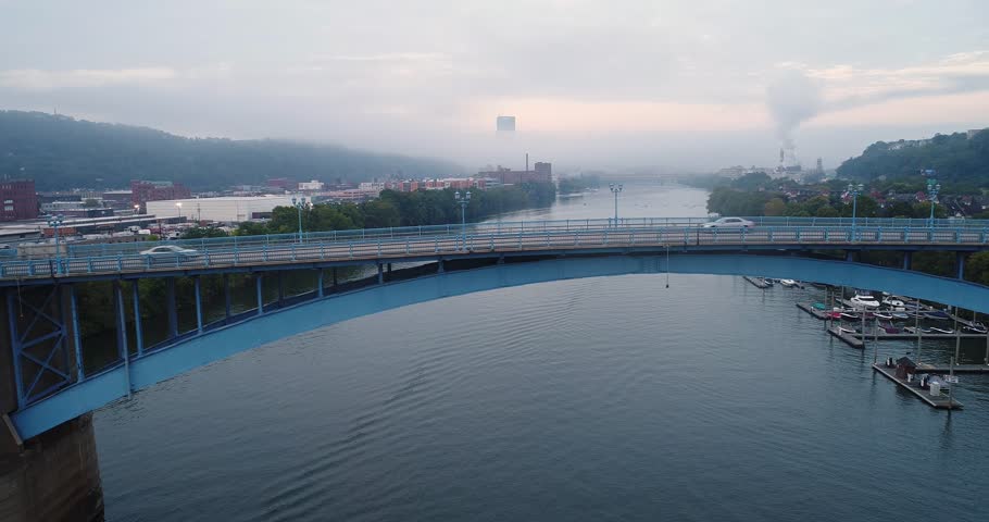 An early morning wide profile aerial establishing shot of traffic passing over the 31st Street Bridge with the foggy Pittsburgh skyline in the distance.  	