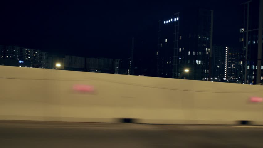 Transport infrastructure, road fence for noise reduction in residential area. View from side window of auto moving with high speed in nighttime, slow motion, empty road in midnight in modern megapolis