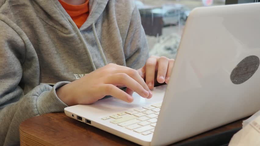 teenage boy wears casual clothes sits alone at table in coffee shop cafe restaurant indoors work or study on laptop pc computer use cell phone. Freelance mobile office business. runs social networks.