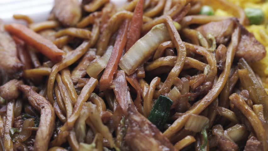Extreme close up of Chinese lo mein noodles served along fried rice and an egg roll