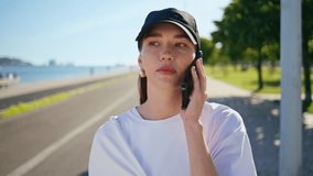 Relaxed brunette talking mobile phone walking sunny city road closeup. Calm young woman calling cellphone strolling by green park alone. Carefree girl in cap speaking smartphone discussing news on go. - Powered by Shutterstock - Get 15% off with code: PIKWIZARD15
