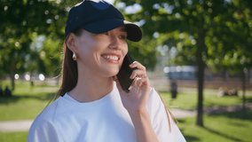 Sporty girl talking cellphone in green park closeup. Cheerful woman wearing casual cap calling smartphone enjoying vibrant summer day outdoors. Beautiful brunette discussing news by mobile phone. - Powered by Shutterstock - Get 15% off with code: PIKWIZARD15
