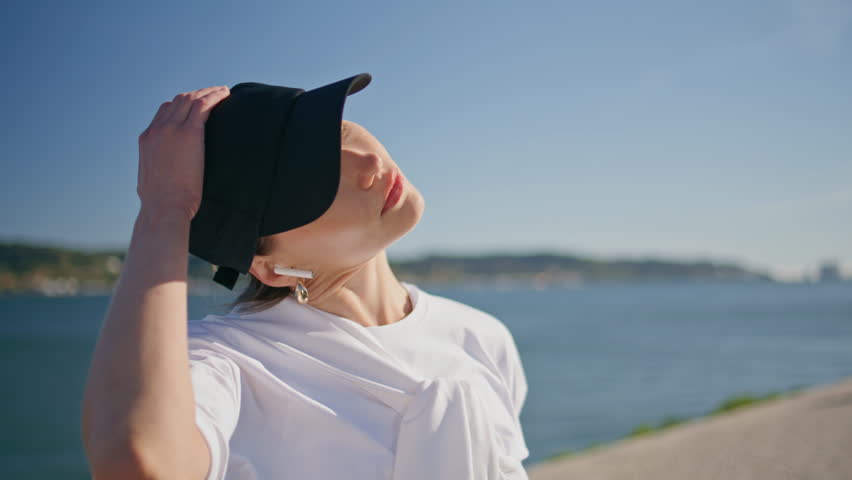 Closed eyes sportswoman stretching neck at sunny riverbank closeup. Serious woman athlete making sport exercises at summer morning outdoors. Active girl enjoy fitness workout wearing wireless earbuds.