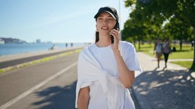 Walking girl talking smartphone enjoying beautiful summer day outdoors closeup. Smiling woman wearing cap calling cellphone strolling sunny street. Happy brunette have mobile phone conversation on go. - Powered by Shutterstock - Get 15% off with code: PIKWIZARD15
