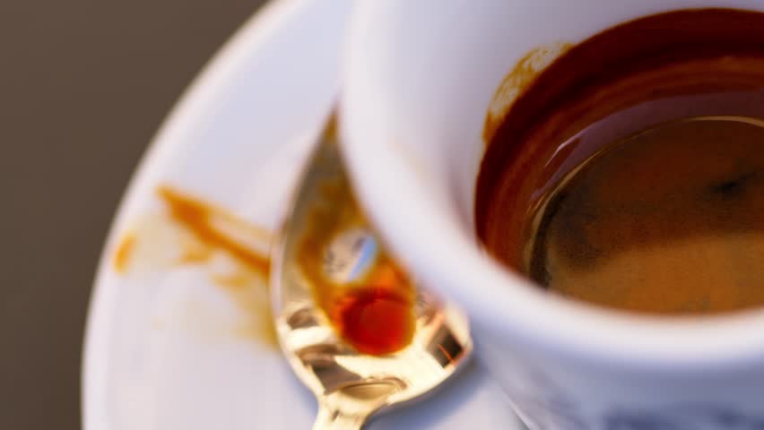 Macro panning shot of espresso cup with a spoon beside it in a cozy cafe setting