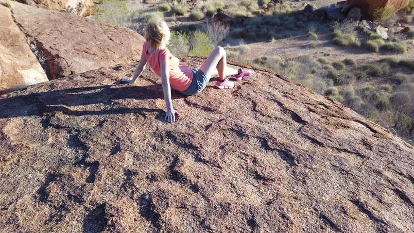 Tourist woman on the top of Karlu Karlu Devils Marbles Conservation Reserve looking panoramic views of granite boulders rock formations at sunset with sunrays of outback. Northern Territory, Australia
