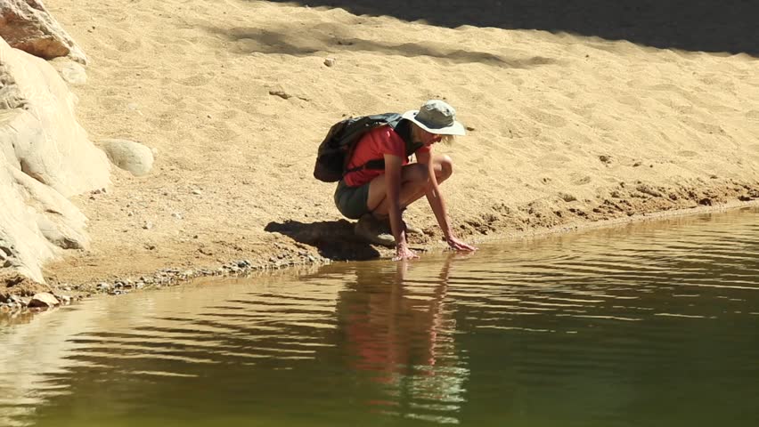 Backpacker woman resting on lake of Ormiston Pound Walk, a circuit that follows the rocky slope of pound and back along the gorge by main waterhole.West MacDonnell Range, Australia, Northern Territory