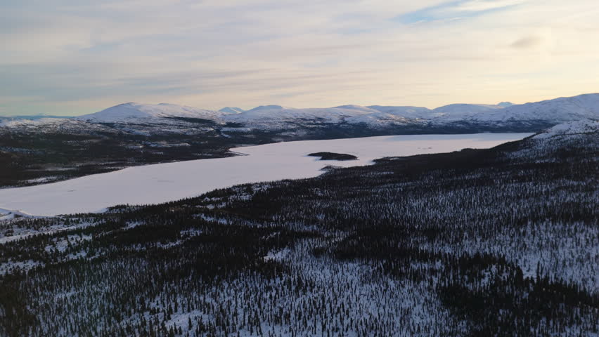 A cinematic sunset aerial shot over Fish Lake and snow-capped mountains near Whitehorse, Yukon, showcasing the untouched beauty and tranquility of Canada