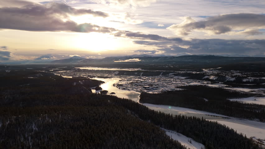 A smooth aerial shot of the rugged Yukon landscape at sunset, highlighting Downtown Whitehorse and the winding Yukon River in this breathtaking view of the northern wilderness.