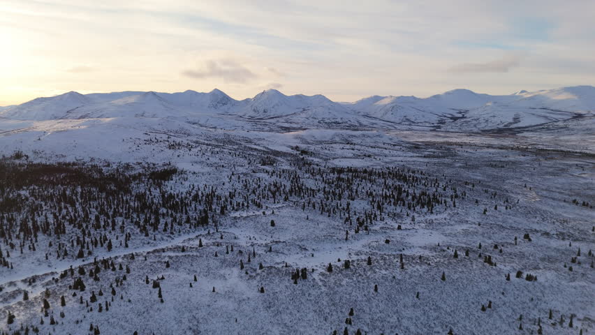 A sweeping cinematic aerial shot of the snowy Fish Lake and surrounding mountain range near Whitehorse, Yukon, offering a breathtaking view of the unspoiled northern wilderness of Canada.