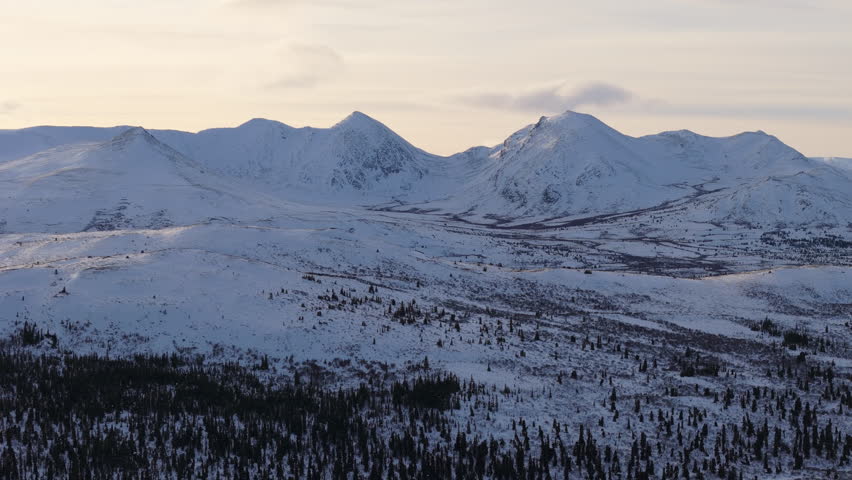 A sweeping cinematic panning aerial shot over snow-covered mountains near Fish Lake near Whitehorse, Yukon, Canada, capturing the untouched beauty of this pristine northern wilderness.