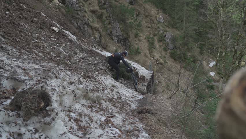 Man cyclist pulls bicycle through avalanche in mountains. Bicyclist is trapped in obstacle and is pulling his cycle through an ice slide with bicycle in his hands. Avalanche on cycling route in Alps. 