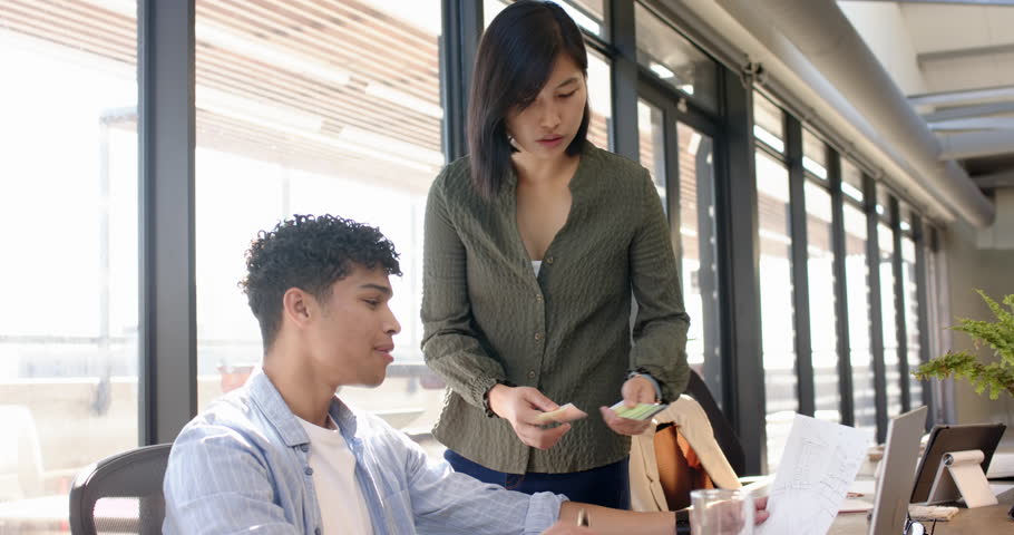 Discussing project, multiracial colleagues using laptop and smartphone in modern office setting. Teamwork, collaboration, technology, business, meeting, workspace