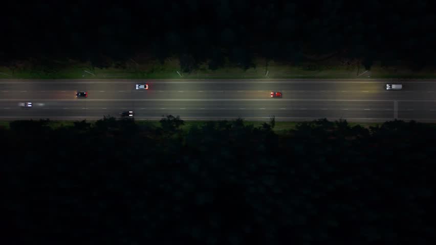 Multiple cars move swiftly on the highway, their headlights illuminating the roadway in the dark. The scene captures a quiet moment of activity against the nighttime backdrop.